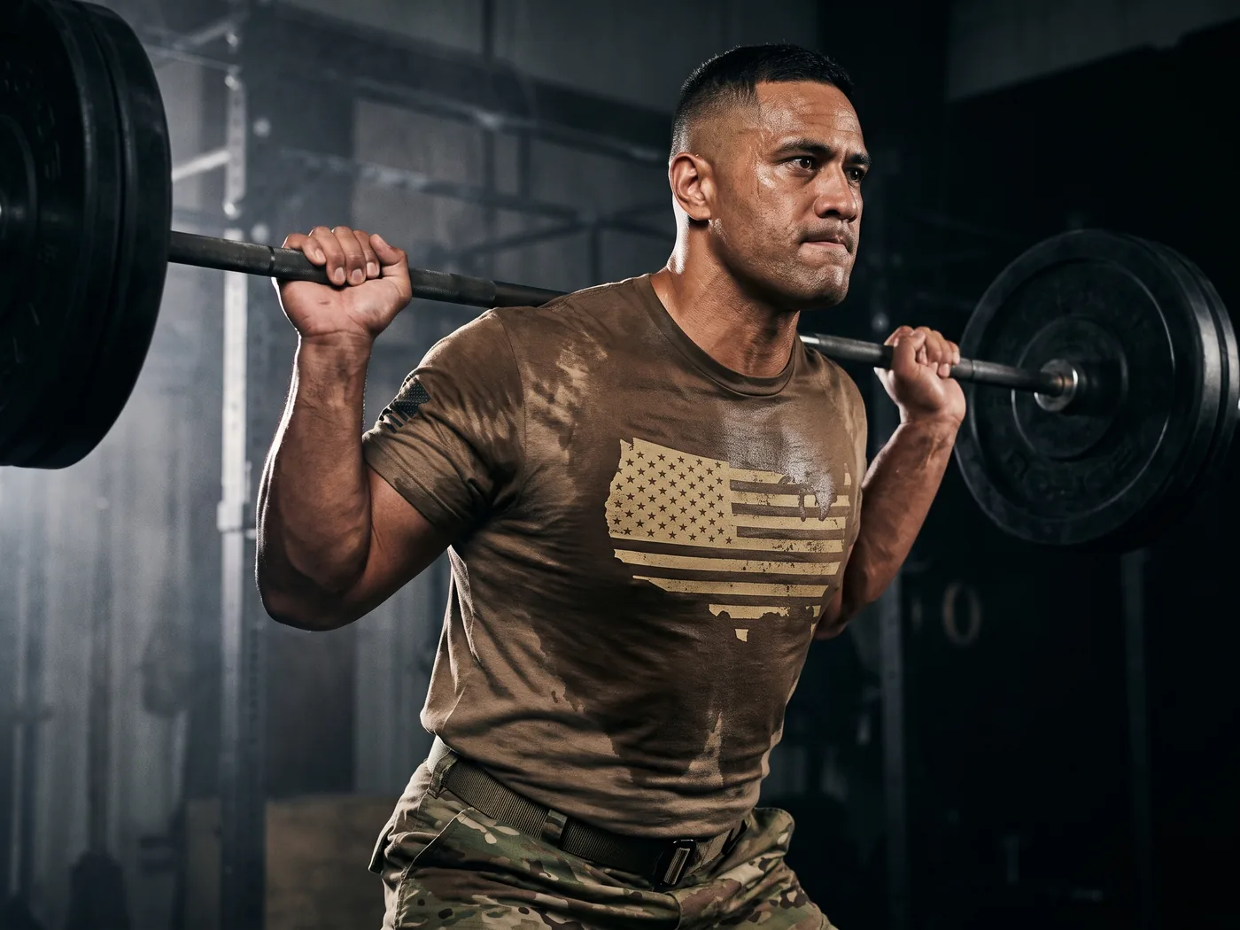 Soldier mid-squat in a gym, sweat revealing the flag print on the covert tee